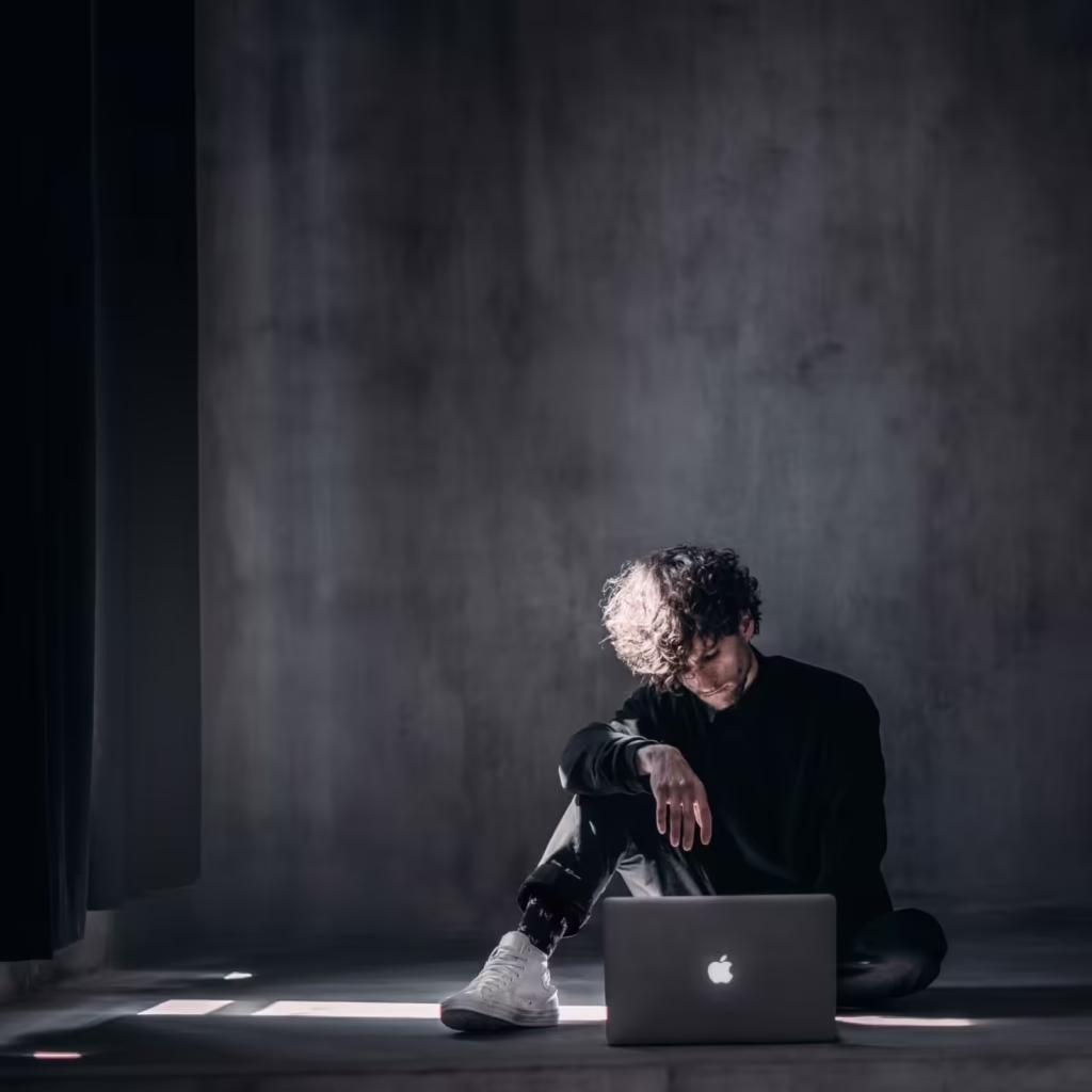 A man sitting on the floor doing a telehealth session on his laptop for addiction treatment